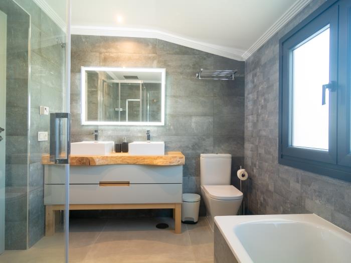 En suite bathroom has a bathtub, a walk-in shower, windows, double sink on wooden stand